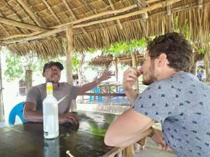 Due uomini seduti a un tavolo con una bottiglia di Mida Creek Nature Camp a Watamu