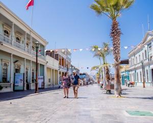 two people walking down a street with a palm tree at Apartamento Alma Capital in Iquique
