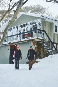 dos personas caminando en la nieve frente a un edificio en Amber Lodge Mt Buller, en Mount Buller