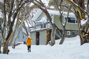 Una donna che cammina nella neve davanti a una casa di Amber Lodge Mt Buller a Mount Buller