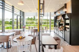 un restaurant avec des tables, des chaises et des fenêtres dans l'établissement B&B HOTEL Igny Palaiseau, à Igny