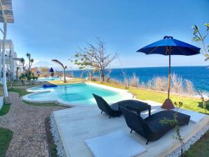 a pool with chairs and an umbrella next to the ocean at Villa Argia Nusa Penida in Nusa Penida