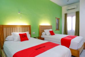 two beds in a room with green walls and red pillows at RedDoorz near Taman Makam Pahlawan Tatura in Palu