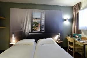 a bedroom with two beds and a desk and a window at B&B HOTEL La Rochelle Angoulins in Angoulins-sur-Mer