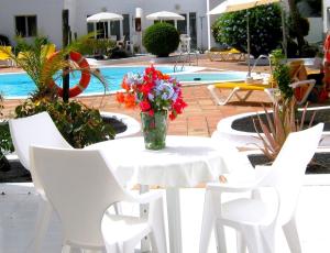 una mesa blanca y sillas con un jarrón de flores. en Apartamentos Tamarindos, en Puerto del Carmen