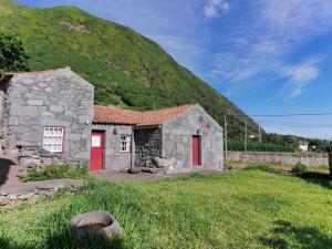 a stone building with red doors in front of a hill at Casas Dos Vimes in Fajã dos Vimes