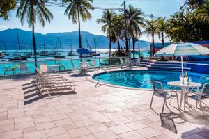 a pool with chairs and a table with an umbrella at Hotel Ilhabela in Ilhabela