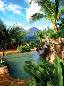 a resort with a waterfall and palm trees and a mountain at The Springs Resort & Spa at Arenal in Fortuna