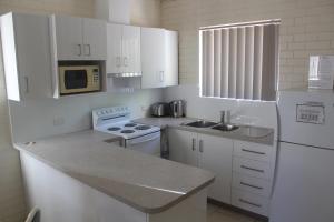 - une cuisine blanche avec évier et four micro-ondes dans l'établissement API Pelican Beach Front Apartments Kalbarri, à Kalbarri