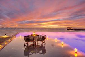 a infinity pool with a table and chairs at sunset at Kudadoo Maldives Private Island &ndash; Luxury All inclusive in Lhaviyani Atoll