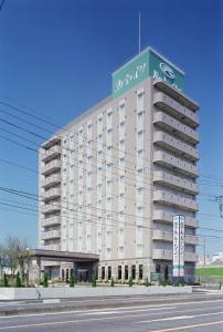 a large white building with a green sign on it at Hotel Route-Inn Shibukawa in Shibukawa