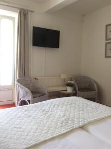 a bedroom with a bed and two chairs and a television at Hotel Pension Oranje in Valkenburg