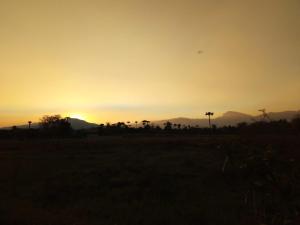 a sunset in a field with mountains in the background at BaanSunlomjoy in Chom Thong