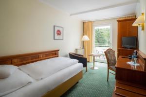 a hotel room with a bed and a desk and a television at Parkhotel am Taunus in Oberursel