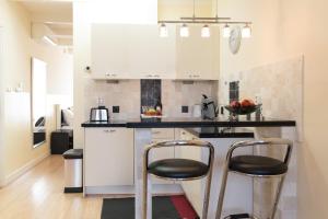 una cocina con armarios blancos y 2 taburetes en B&B Canaliscious, en Ámsterdam