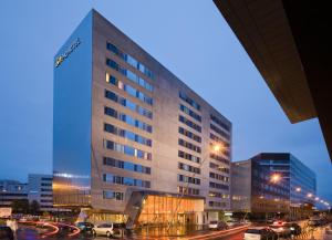 Un grand bâtiment avec des voitures garées dans un parking dans l'établissement Novotel Suites Lille Europe, à Lille