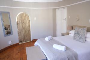 a white bedroom with a bed and a mirror at Amber Light Wilderness Beach Cottage in Wilderness