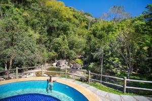 a woman standing in a swimming pool in front of a forest at Eco Resort Hotel Villa São Romão in Lumiar