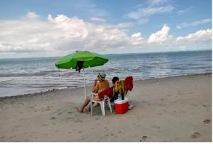 dos personas sentadas bajo un paraguas en la playa en Casa Ilha de Itaparica, en Itaparica