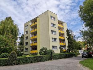 a tall apartment building with yellow windows and bushes at Poza zgiełkiem miasta, a jednak wszystko w zasięgu in Bydgoszcz