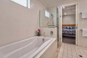 a white bathroom with a tub and a bedroom at Pavillions on Hamilton Island in Hamilton Island