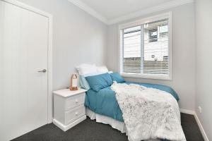 a white bedroom with a blue bed and a window at The Weiti Waterfront in Whangaparaoa