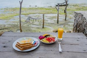 a table with two plates of breakfast foods and a glass of orange juice at Wooden Beach Sunset Cottages in Nusa Lembongan