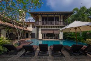 a swimming pool with chairs and an umbrella next to a house at Sergeant House Boutique Villa & Private Beach in Unawatuna