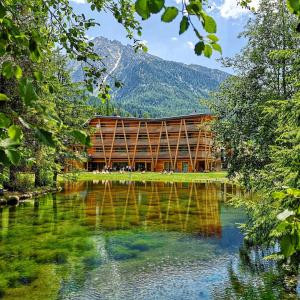 a building next to a lake with a mountain at Au Charmant Petit Lac - Ecohotel Parc & Spa in Champoluc