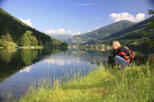 a person with a backpack sitting next to a lake at Ferienwohnung Villa Heinrich in Feld am See