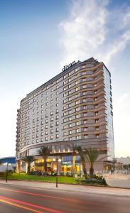 a large hotel building with palm trees in front of a street at Divan Mersin in Mersin