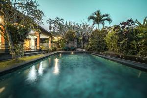 a swimming pool in front of a house with trees at Nyoman Sandi Guest House in Ubud