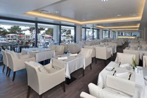 a restaurant with white tables and chairs and windows at Hotel Parentium Plava Laguna in Poreč