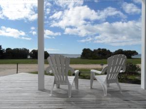 Dos sillas blancas sentadas en un porche con vistas al océano en WHITE SHELLS HOLIDAY RENTAL, en Nepean Bay