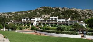 a large white building with a mountain in the background at Hotel La Bisaccia in Baja Sardinia