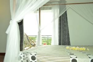 Schlafzimmer mit einem Bett mit weißen Vorhängen und einem Fenster in der Unterkunft Villa Malandy Appart Hôtel Triplex in Madirokely