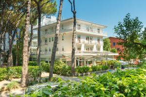 een groot wit gebouw met bomen ervoor bij Hotel Milano in Eraclea Mare