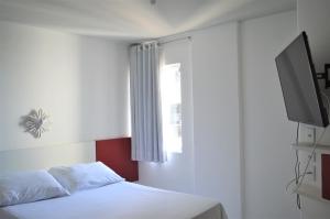 a bedroom with a white bed and a television at Apart Cote D'Azur Maceió in Maceió