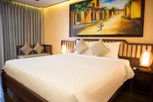 a bedroom with a white bed and a painting on the wall at Fivitel Hoi An Hotel in Hoi An