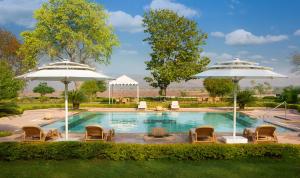 a swimming pool with chairs and umbrellas at Ramgarh Lodge, Jaipur – IHCL SeleQtions in Jaipur