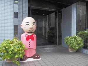 Eine Statue eines Mannes in Anzug und Fliege neben Pflanzen. in der Unterkunft Hotel Tetora Makuhari Inagekaigan (Formerly Business Hotel Marine) in Chiba