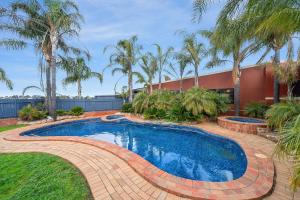 a swimming pool in a yard with palm trees at Peppermill Inn Motel in Shepparton