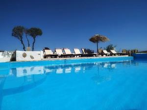 a pool of blue water with chairs and umbrellas at Anatoli Studios in Schinoussa