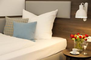 a bed with white pillows and a table with flowers at Lizz Hotel Munich in Munich