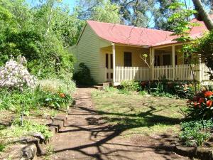 ein gelbes Haus mit rotem Dach und einem Garten in der Unterkunft Hermitage Cottage in Kurrajong