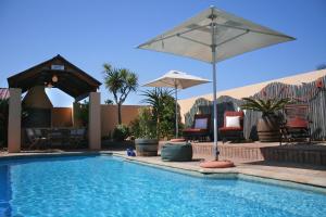 uma piscina com guarda-sol, cadeiras e mesas em Avenues Guesthouse em Mossel Bay