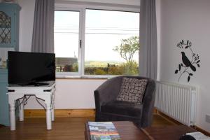 sala de estar con silla, TV y ventana en Madra Rua Organic Accommodation, en Ballyliffin