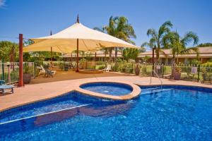 a swimming pool with an umbrella next to a house at Paradise Lakes Motel Shepparton in Shepparton