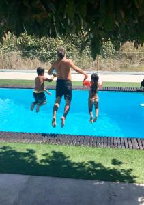 a man and two children jumping into a swimming pool at Laurel Beach House in Lourinhã