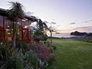 a house with a garden in front of the ocean at Bethells Beach Cottages in Bethells Beach